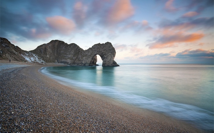 Durdle Door rock arch on a pebble beach at sunrise