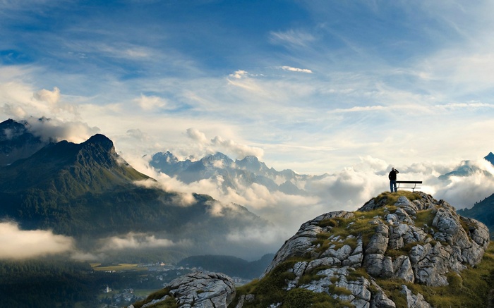Man on mountain top with bench overlooking clouds