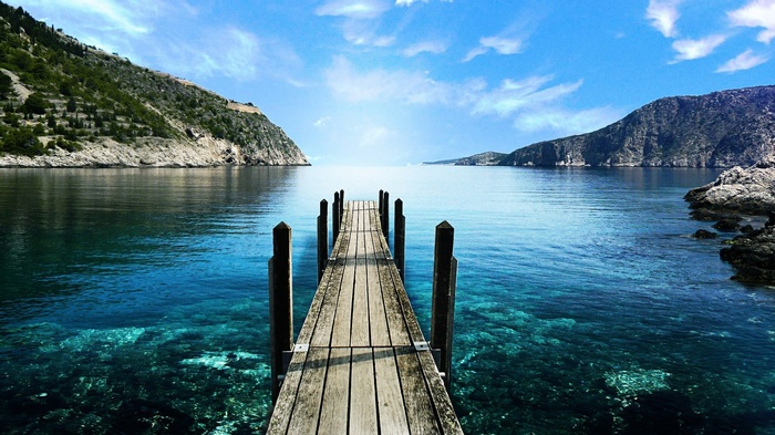 Wooden pier on a clear blue sea with mountains