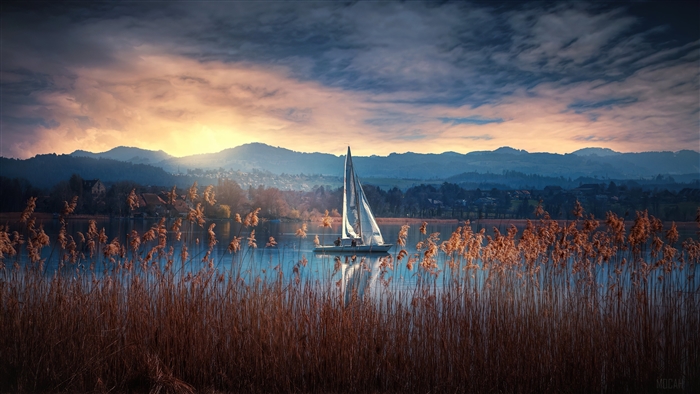 Sailboat on a lake at sunrise with mountains