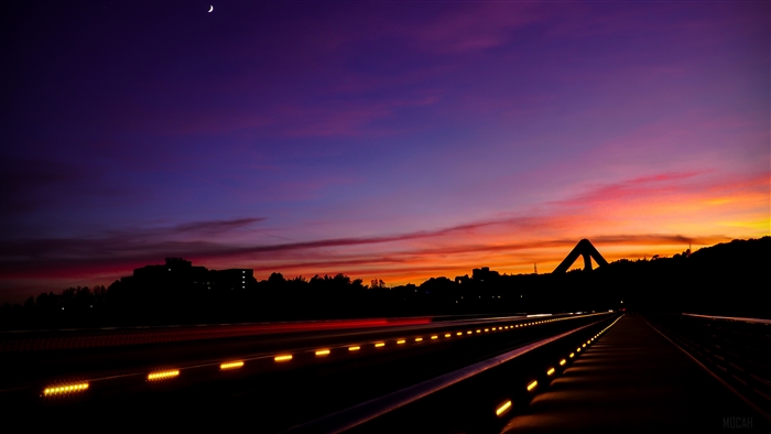 Sunset over a road with light trails and a bridge