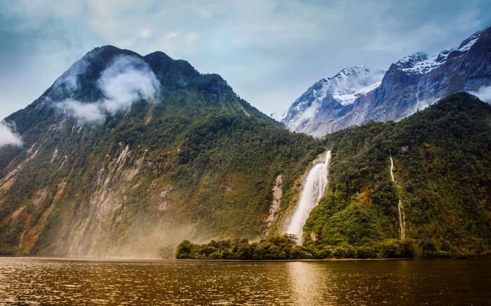Waterfall cascading down a lush green mountain into a lake