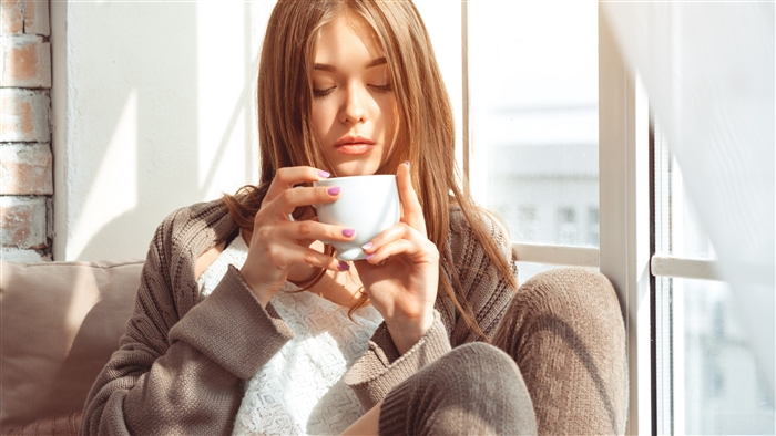 Young woman drinking from a mug by the window