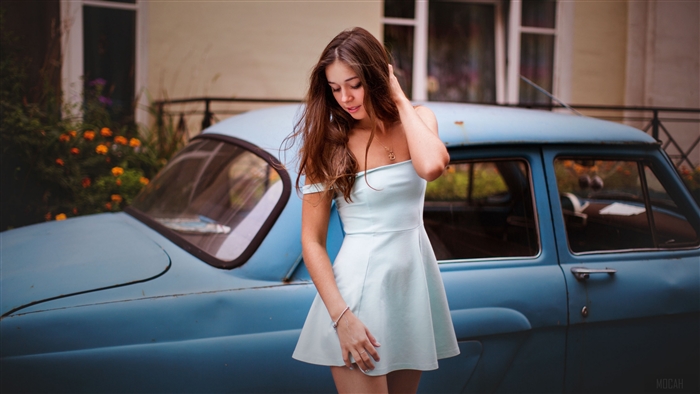Young woman in a light blue dress next to a vintage car