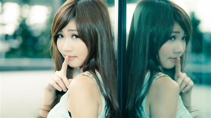 Young woman with finger to lips in front of reflective surface