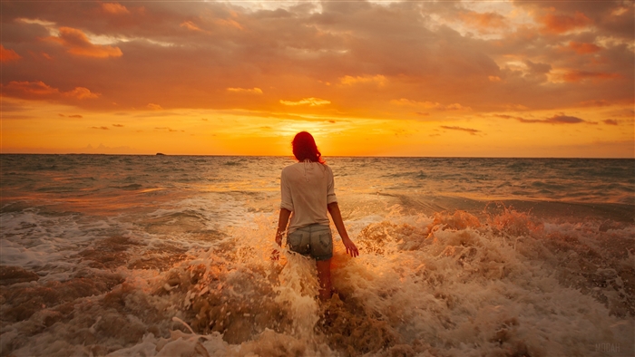 Woman walking into the ocean at sunset