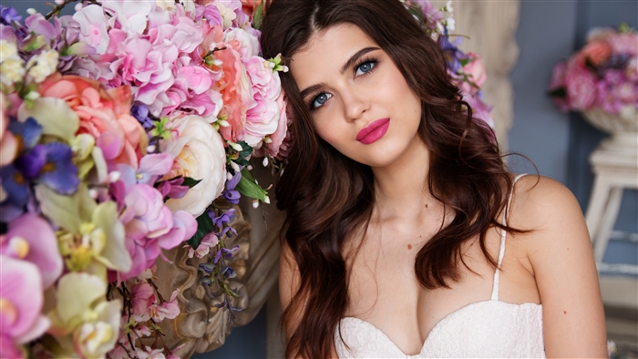 Brunette woman with blue eyes and pink lipstick near flowers