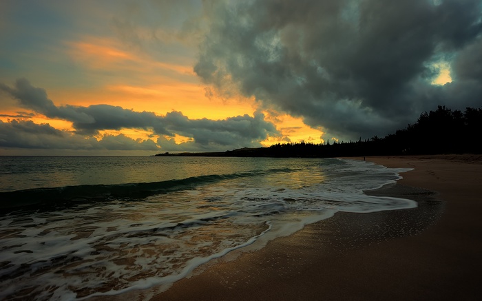 Sunset over a beach with dark clouds and ocean waves