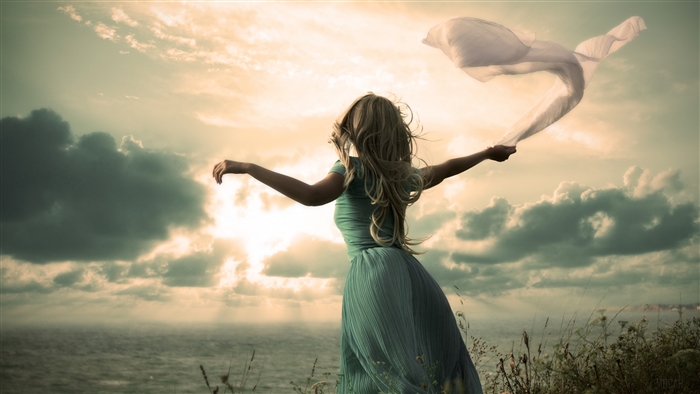 Woman with flowing scarf on cliff overlooking ocean