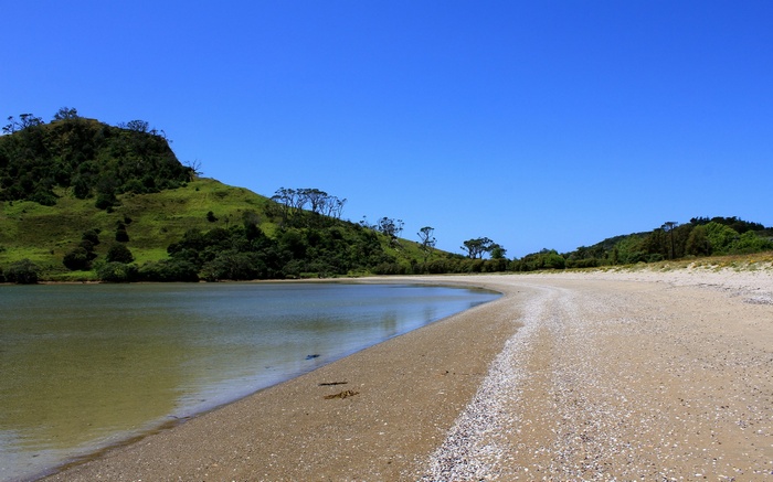 Sandy beach with calm water and green hills under blue sky