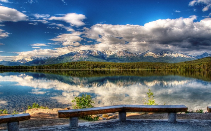 Wooden benches overlook a calm lake with mountains and forest