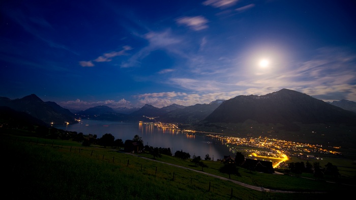 Town lights reflecting on a lake at night with mountains