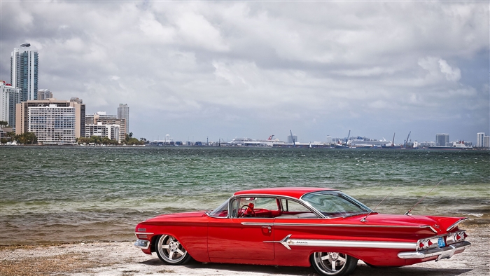 Red Vintage Car on Beach with City Skyline