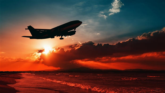 Airplane taking off over the ocean at sunset