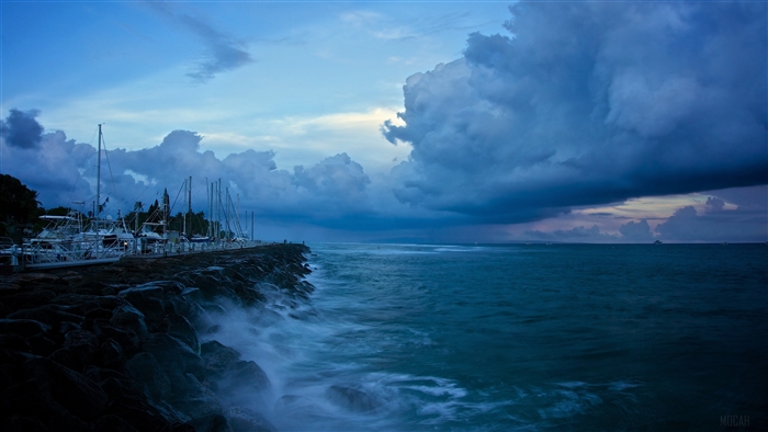 Boats docked at a rocky coastline under stormy blue clouds