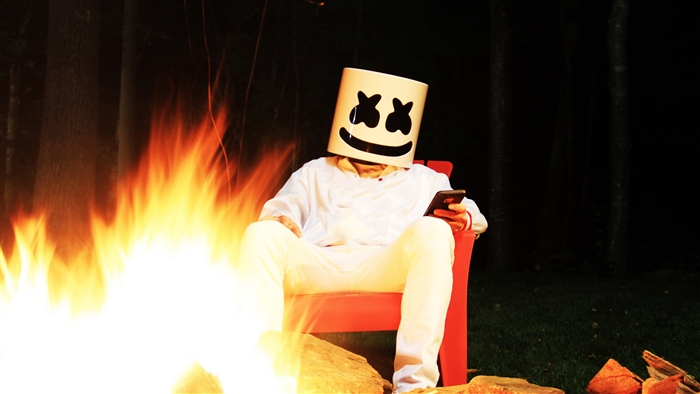 Marshmello sitting by a campfire at night