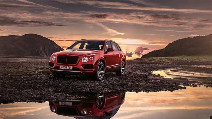 Red Bentley Bentayga SUV parked by water at sunset