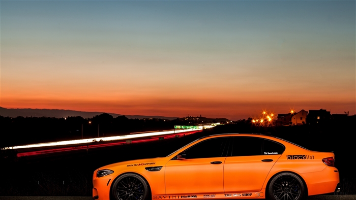 Orange BMW M5 with Blacklist sticker on highway at sunset