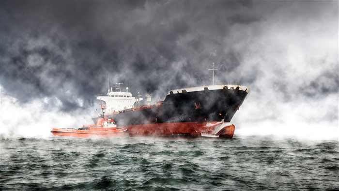 Tugboat assisting a tanker ship in foggy ocean