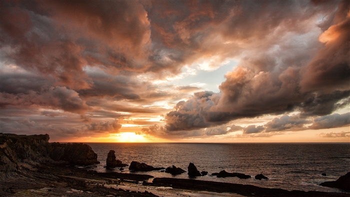 Sunset over the ocean with dramatic clouds and rocky shore
