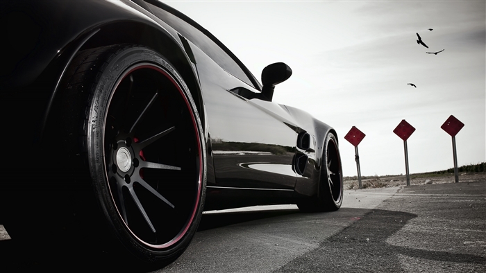 Black sports car on a road with red signs