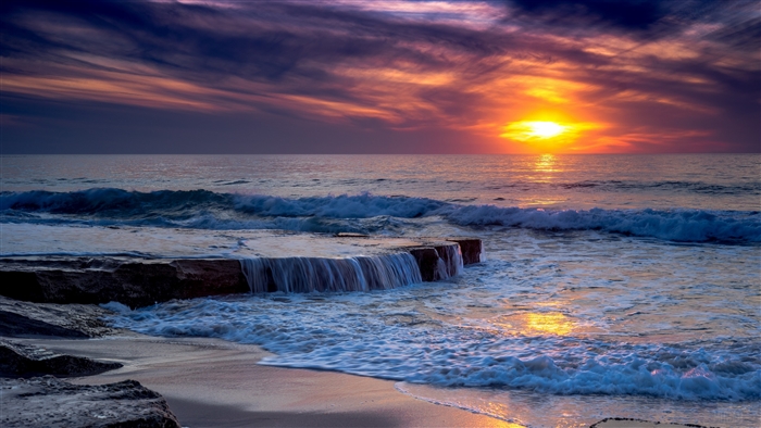 Sunset over the ocean with waves crashing on rocks