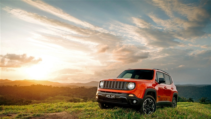 Orange Jeep Renegade SUV on a grassy hill at sunset