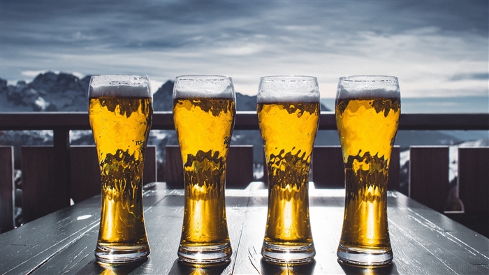 Four glasses of beer on a table with mountains in the background 4K