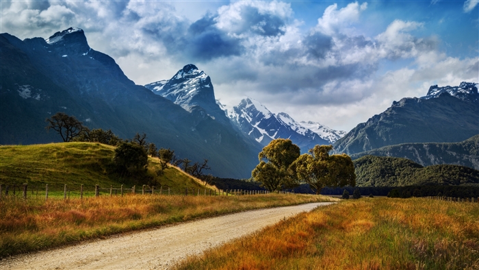 Dirt Road Through Grassy Field Towards Snow-Capped Mountains