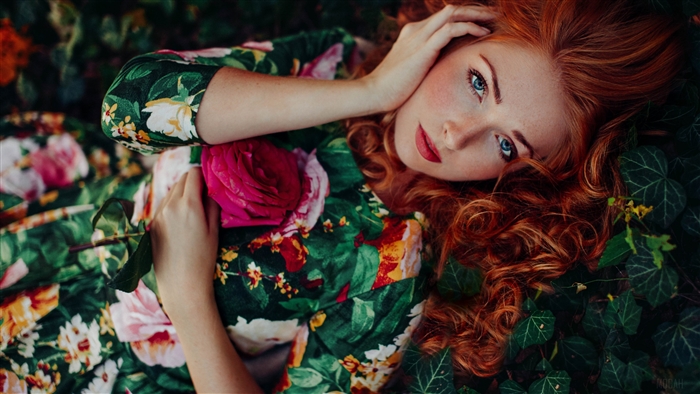 Redhead woman with blue eyes lying down with a rose