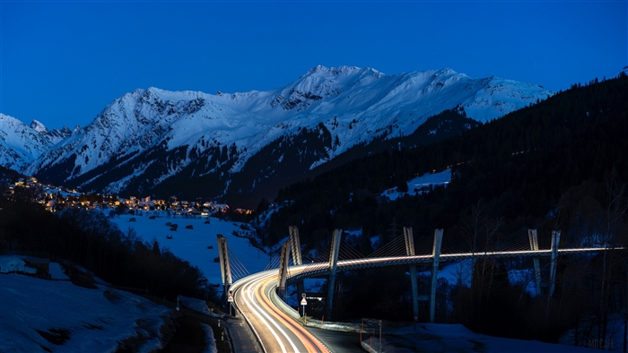 Bridge with light trails in snowy mountains at night