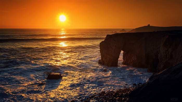 Sunset over the ocean with a coastal arch