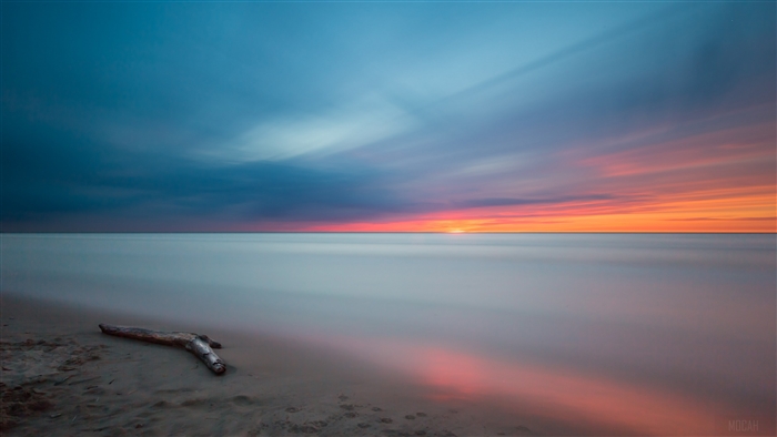 Sunset over the ocean with driftwood on sand 4K
