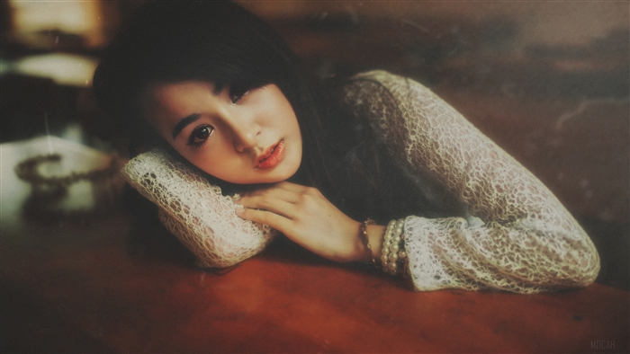 A young woman in a lace top rests her head on her arms