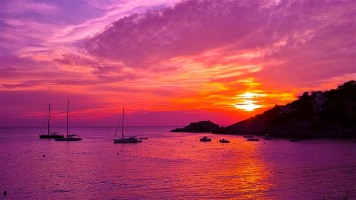 Boats in the ocean during a purple and orange sunset in Ibiza, Spain 4K