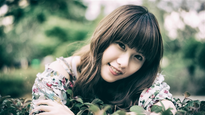 A young woman with bangs smiles in a garden