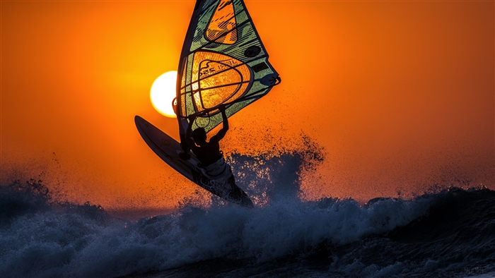 Windsurfer silhouetted against a sunset over waves