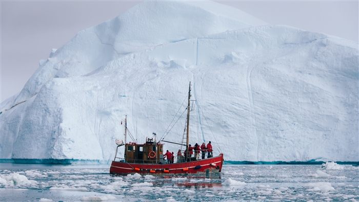 Red boat with people near a large iceberg