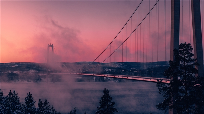 Suspension bridge over a misty river at sunset