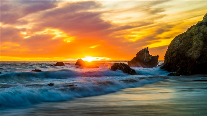 Sunset over the ocean with rocks and waves