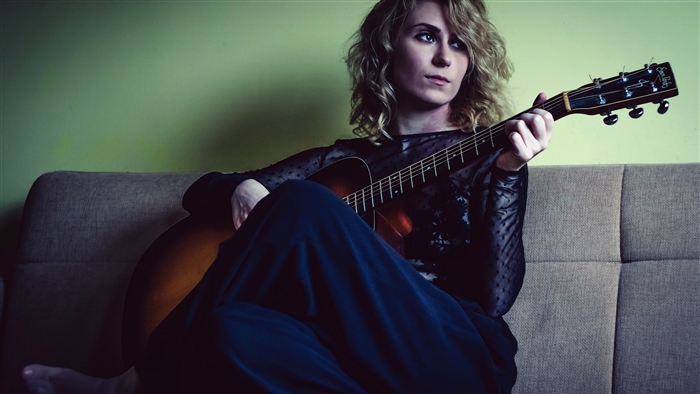 Woman playing acoustic guitar on couch