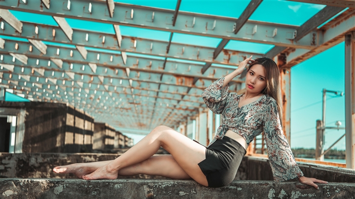 Woman posing on a concrete ledge under a metal structure