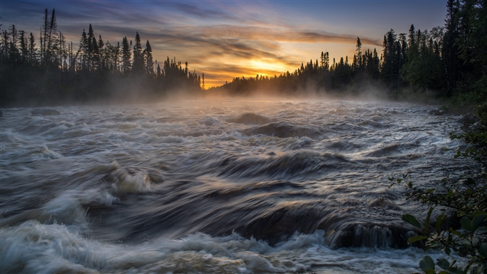 River rapids at sunrise with mist and forest