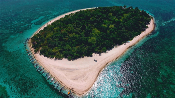 Island with lush trees and boats in turquoise ocean 4K
