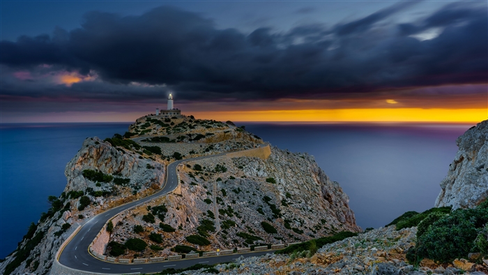 Lighthouse on a rocky coast with a winding road at sunset