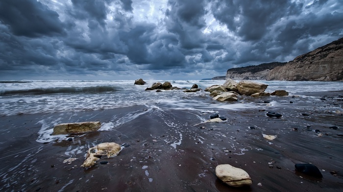 Stormy beach with waves crashing on rocks and dark clouds