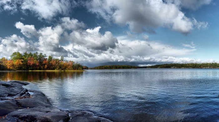 Lake with autumn trees and rocky shore under cloudy sky