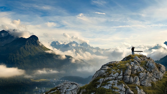 Person on mountain peak overlooking clouds and mountains