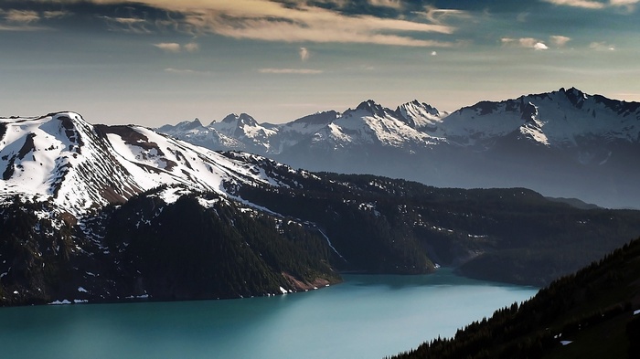Turquoise lake surrounded by snow-capped mountains and dark forests