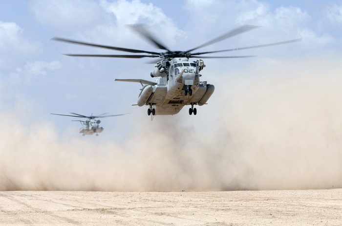 Two military helicopters flying low over a desert